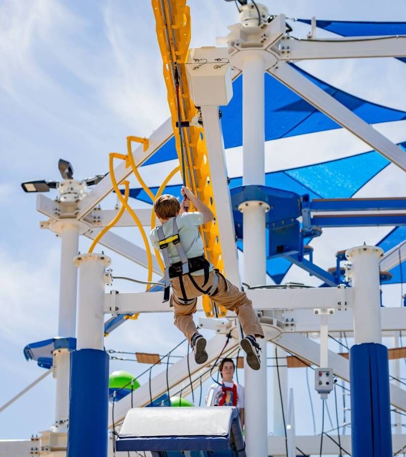 Person suspended on a ropes course at an outdoor adventure park under blue shade sails