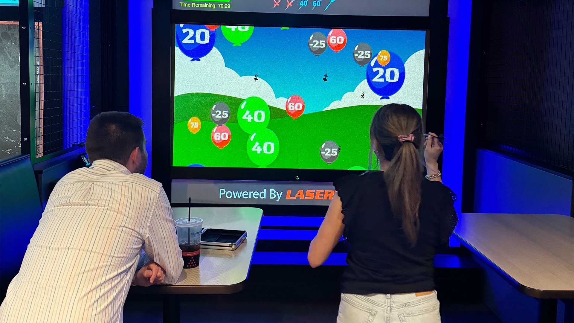 Two people playing a colorful arcade game with numbered targets on a large screen