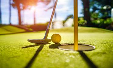 Golf ball and putter beside the hole on a sunlit green course