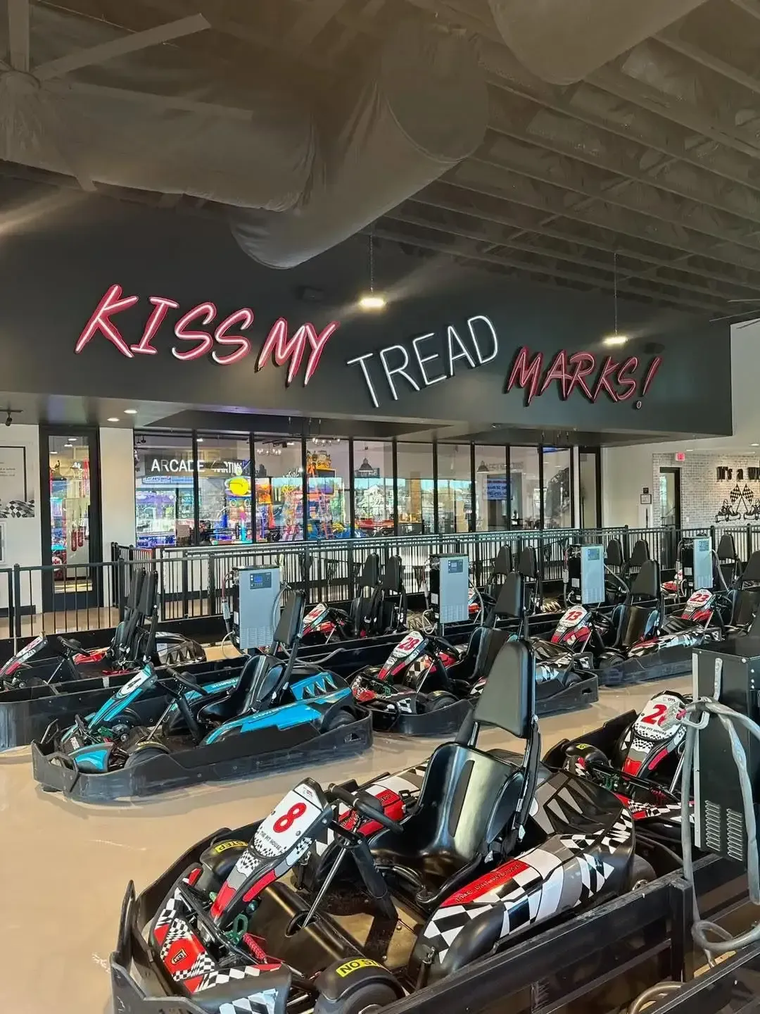 Go-kart showroom with rows of black, red, and blue karts under a “Kiss My Tread” sign