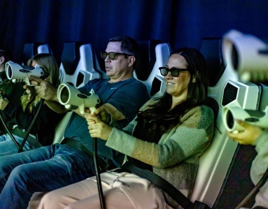 People seated in a dark VR theater, wearing 3D headsets and holding motion controllers