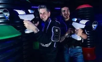 Two people smiling at a neon-lit arcade laser tag scene, aiming white laser tag guns