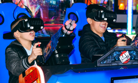 Two people wearing VR headsets and holding controllers in a bright arcade racing game