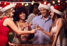 Friends in Santa hats toasting at a festive holiday party with string lights and warm drinks