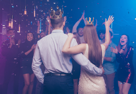 Couple dancing with raised arms at a colorful nightclub party with cheering crowd and confetti