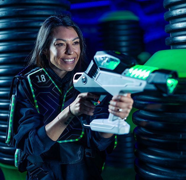 Smiling person aiming a futuristic blaster in a neon-lit arcade arena