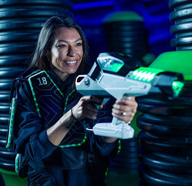 Smiling person aiming a futuristic white-and-green blaster in a neon-lit sci-fi setting