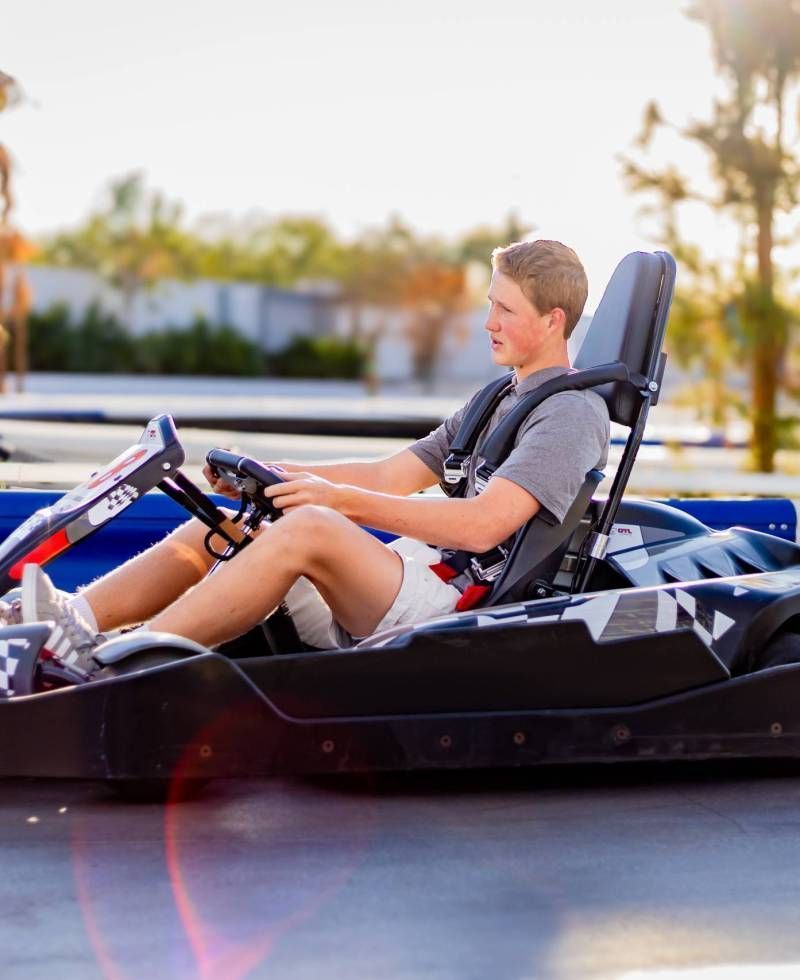 Person sitting in a black go-kart, driving outdoors in bright daylight