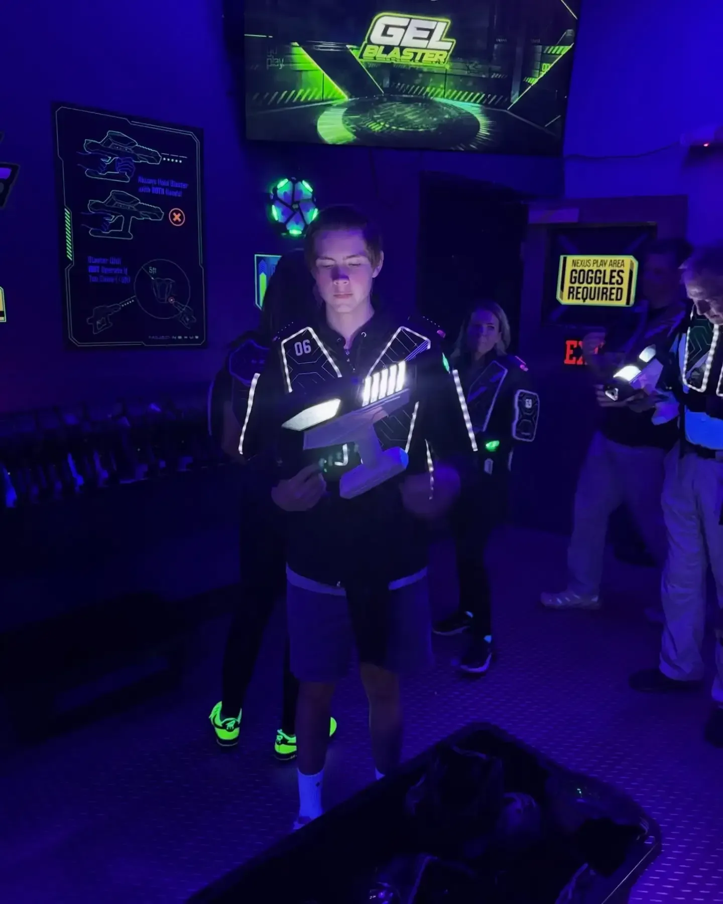 People in glowing vests at a laser tag arena with neon blue and green lighting