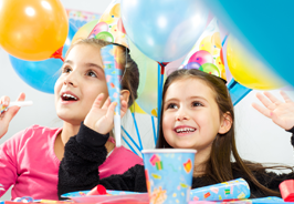 Children at a birthday party, smiling amid balloons and party hats