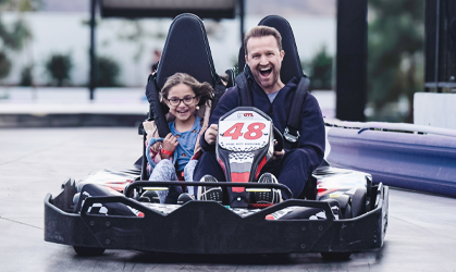 Two people smiling in a go-kart, racing on a track with the number 48 on the front.