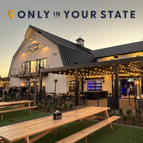 Outdoor restaurant with picnic tables, string lights, and a barn-style building at sunset