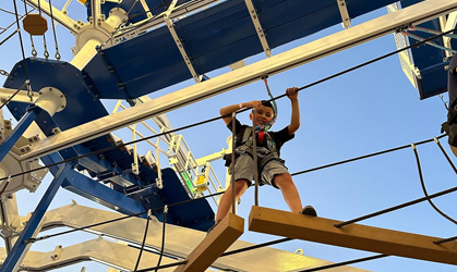 Person balancing on ropes and wooden planks at an outdoor aerial obstacle course, viewed from below