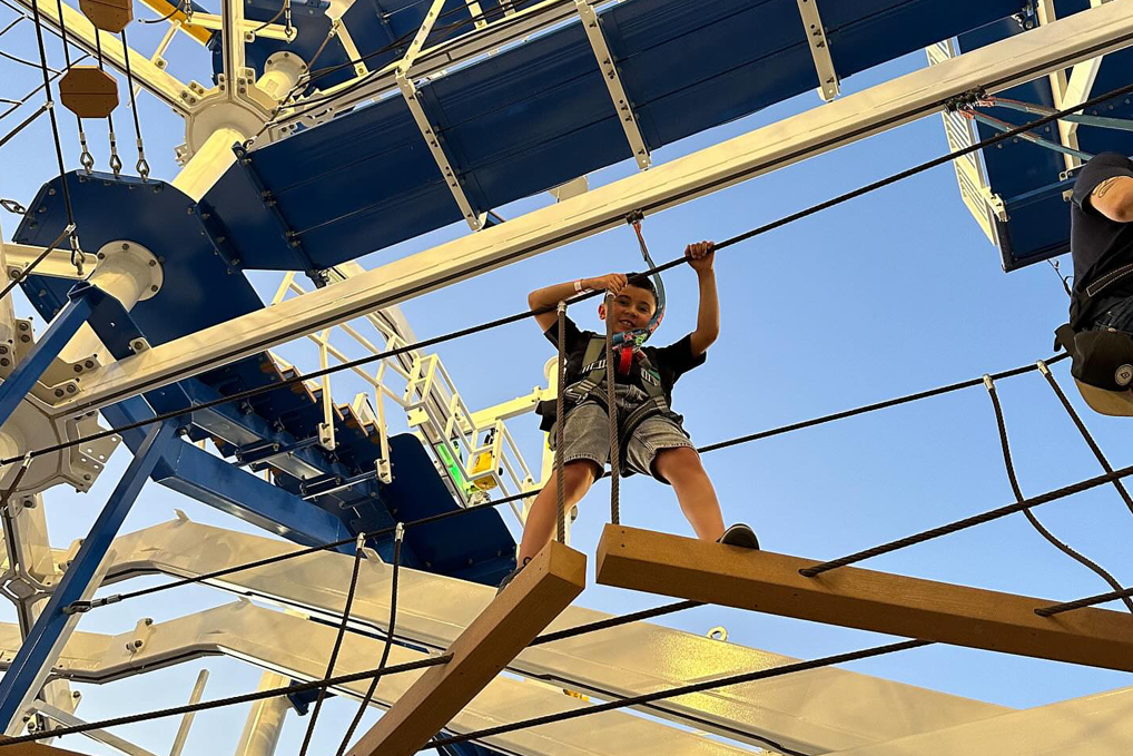 Child climbing ropes on an outdoor adventure course under blue and yellow platforms