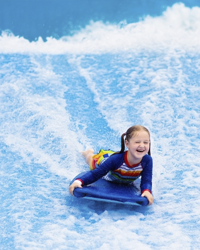 Child smiling while bodyboarding down a blue water slide