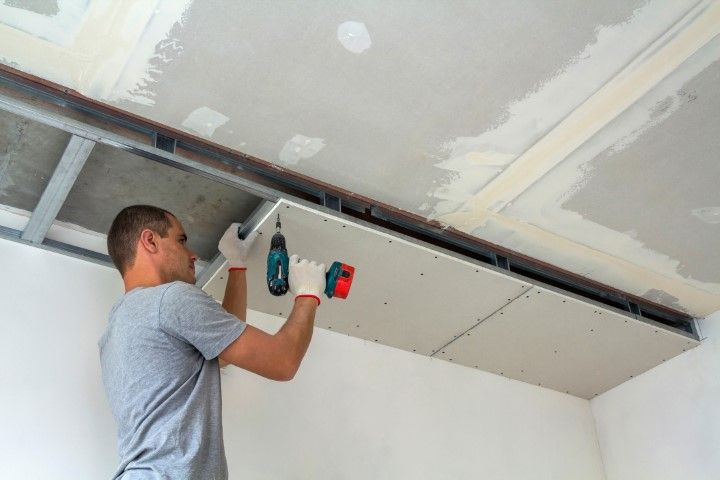 Worker installing a ceiling panel with a drill in an unfinished room