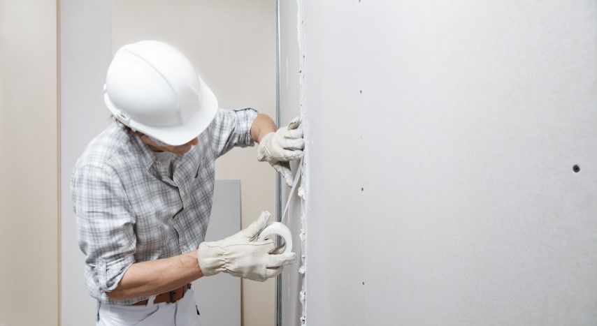 Worker in a hard hat installing wiring inside a wall during construction.
