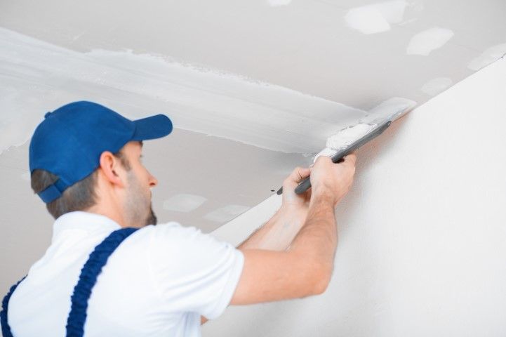 Painter applying white paint to a ceiling with a roller in a room under renovation