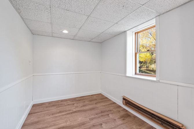 Empty white room with wood flooring, wainscoting, and a window showing autumn trees