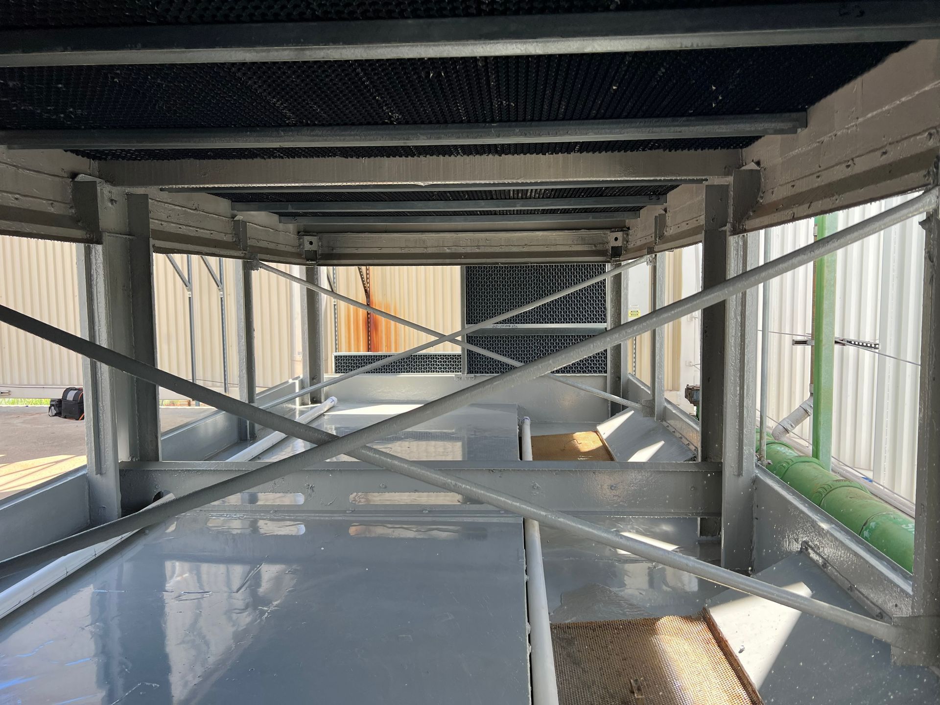 Industrial walkway under construction with metal cross-bracing, reflective floor, and corrugated walls