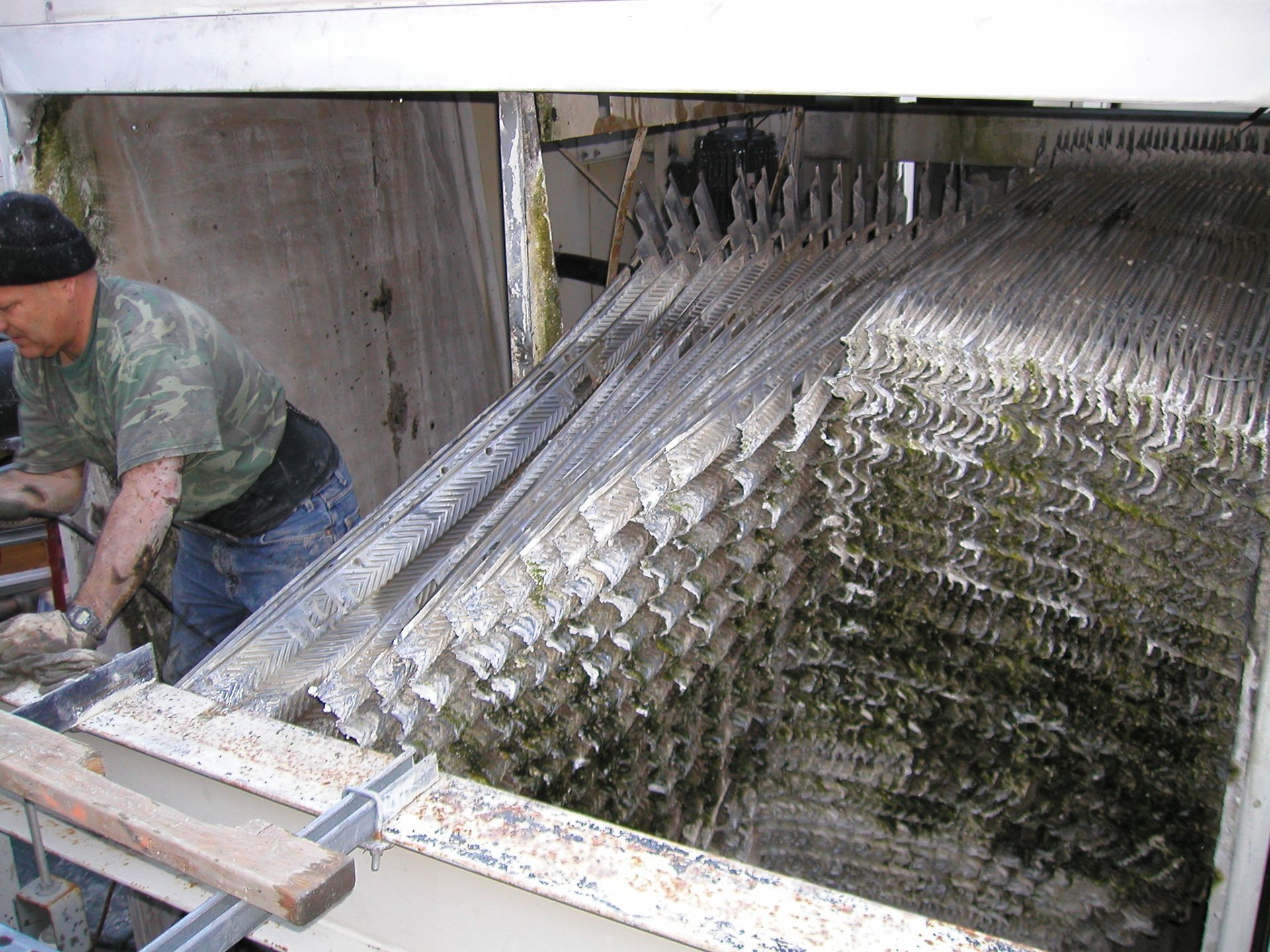 Worker beside a large metal sluice or conveyor covered with ice, in an industrial setting