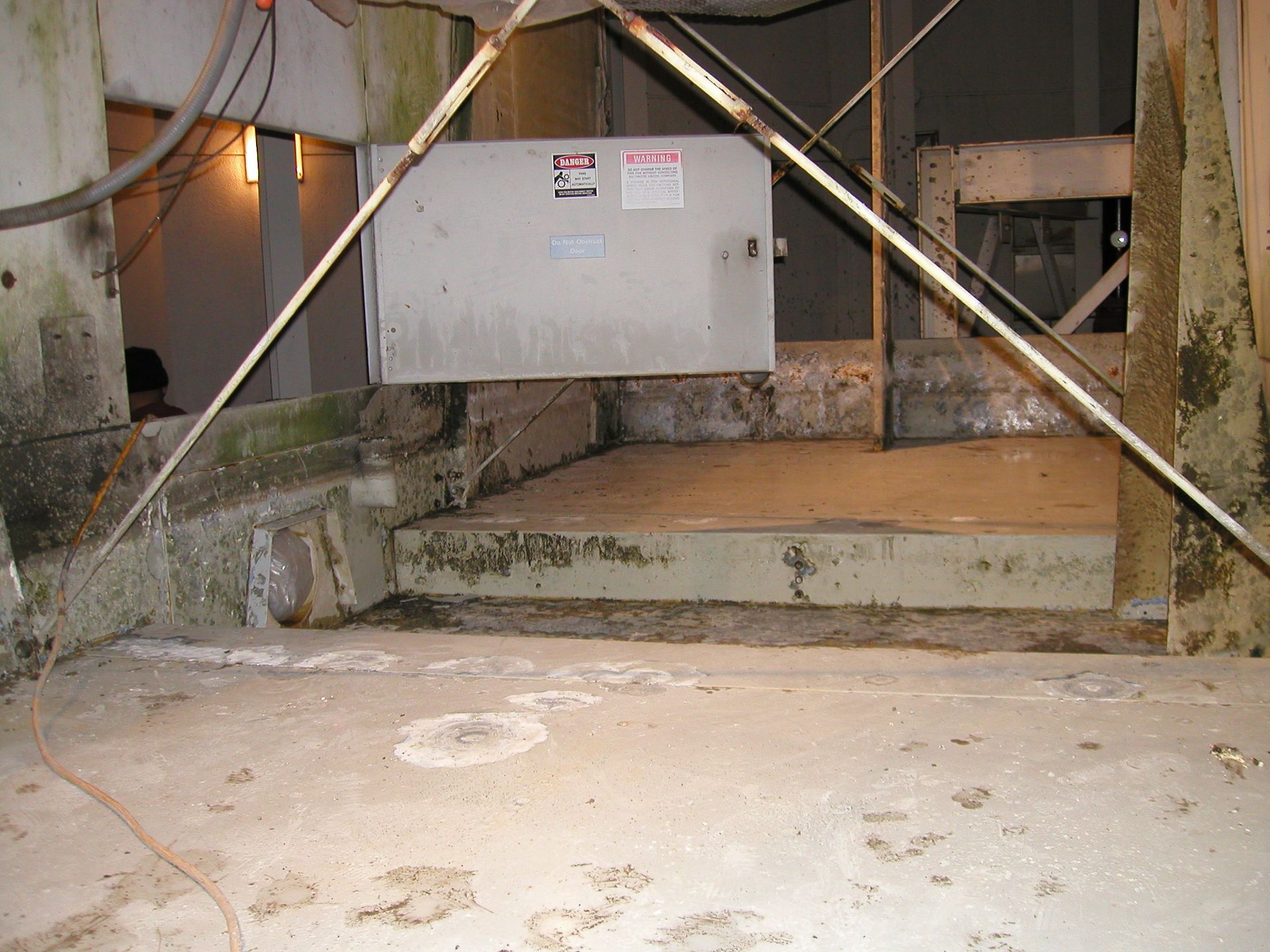 Basement crawlspace with exposed pipes, insulation, and a white electrical box under stairs