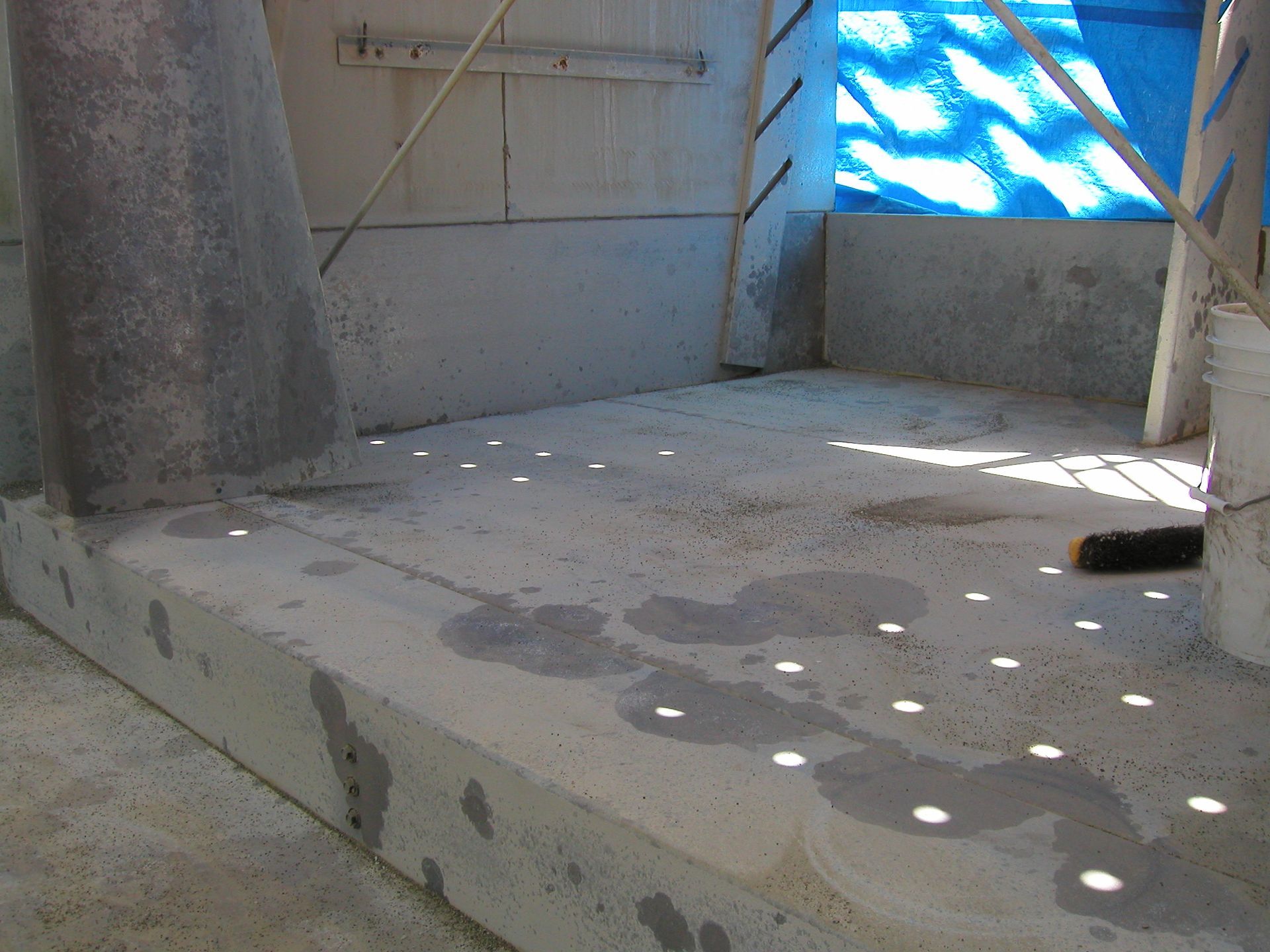 Empty concrete room with sunlight dots on the floor and a blue tarp-covered opening.