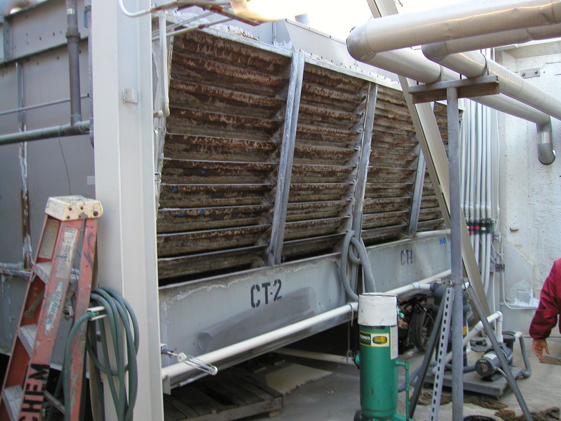 Industrial cooling unit with dusty slanted fins, labeled “CT2,” beside piping and a ladder in a plant area