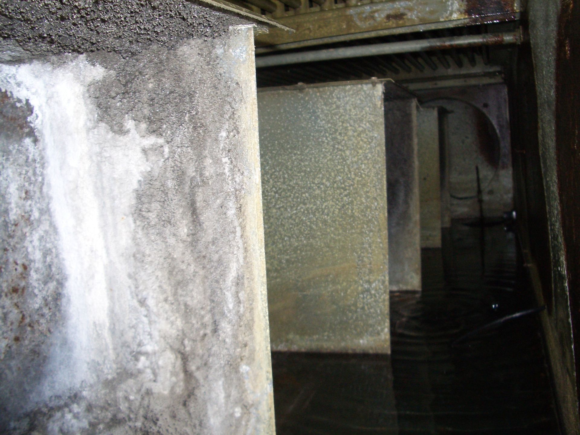 Dark, grimy industrial interior with metal tanks and a narrow walkway in shadow
