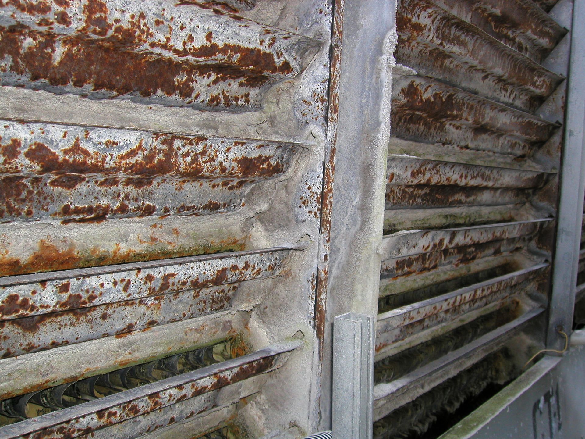 Rusty metal shutters with peeling white paint and a concrete support post.