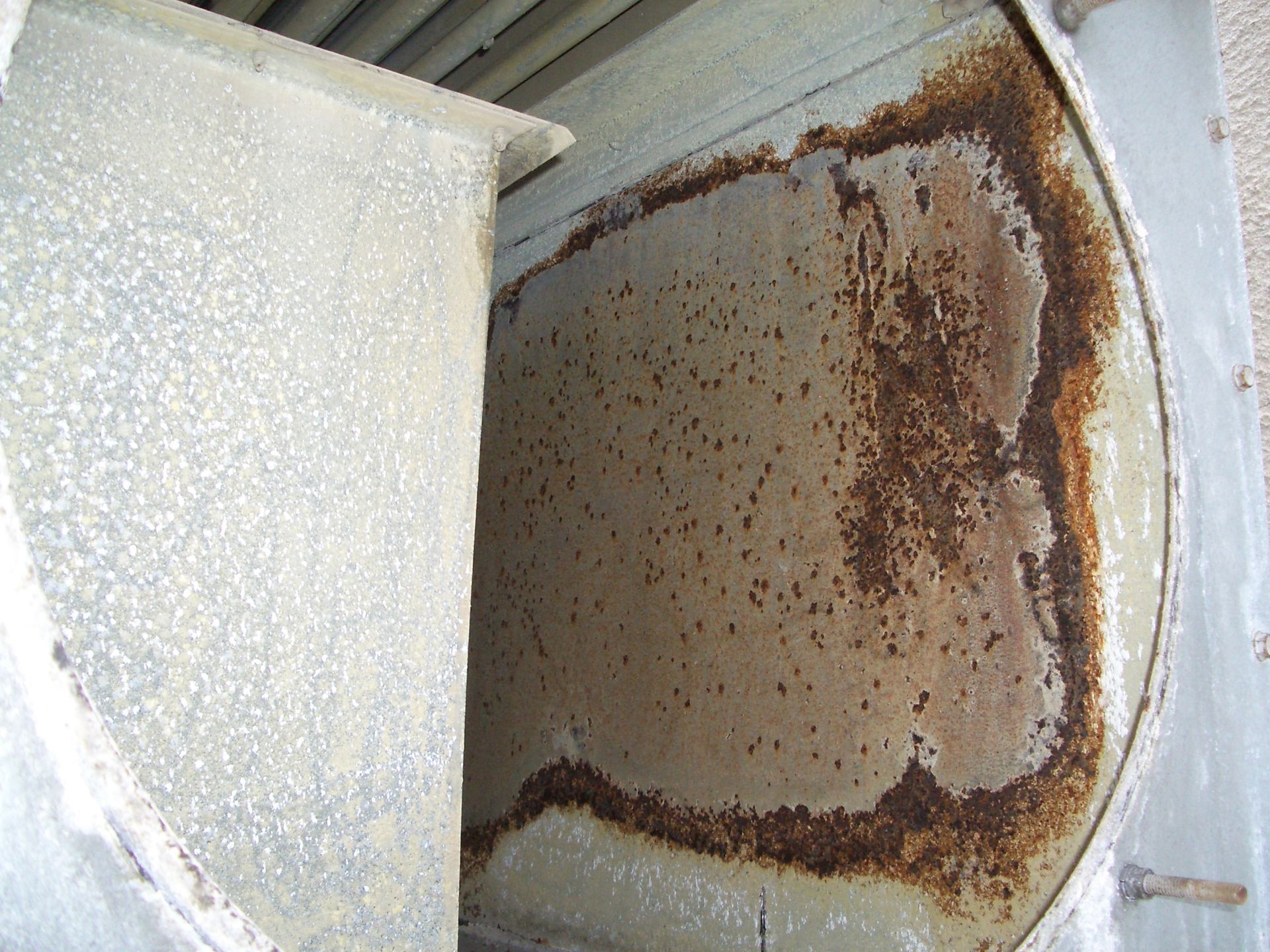 Rusty metal panel with heavy corrosion around the edges inside a white enclosure.