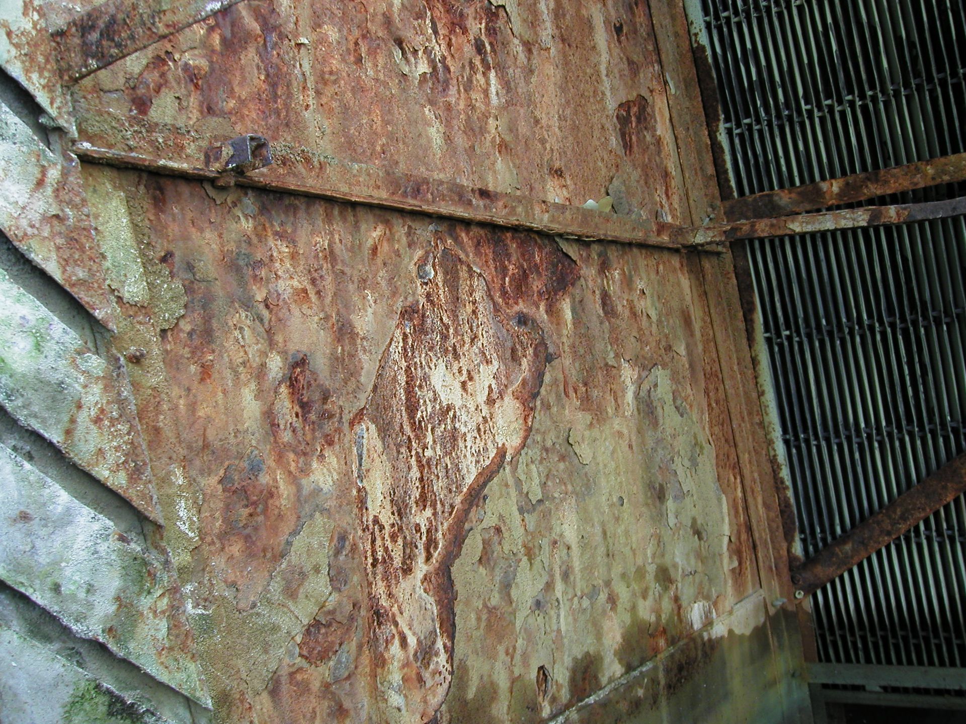 Rusty corrugated metal wall with peeling paint and weathered, diagonal wooden supports