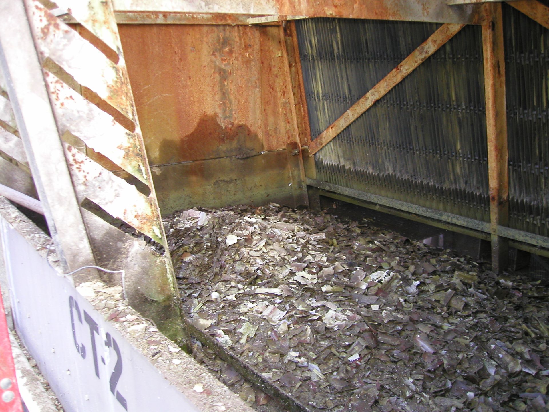 Rusty industrial enclosure with a muddy, debris-covered floor and white striped support beams