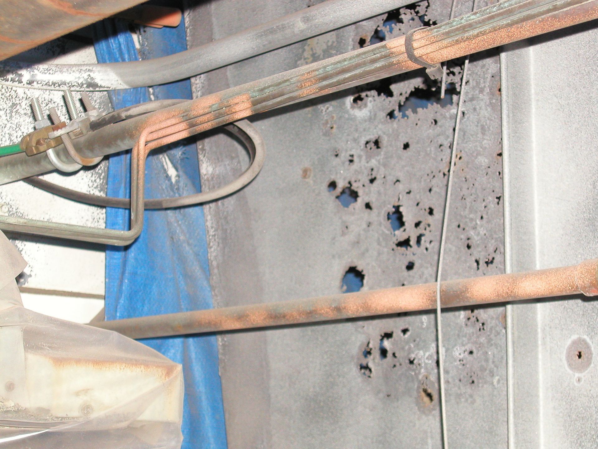Rusty pipes above a metal panel with several holes and black scorch-like marks
