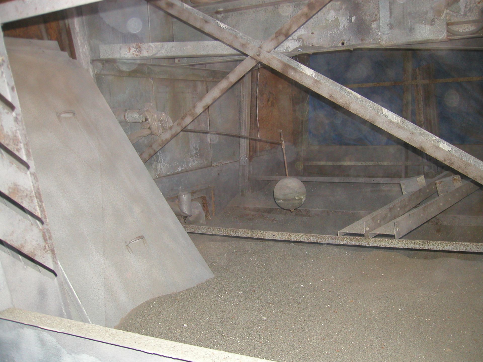 Inside a weathered wooden enclosure, a small round object hangs above a gravel floor.