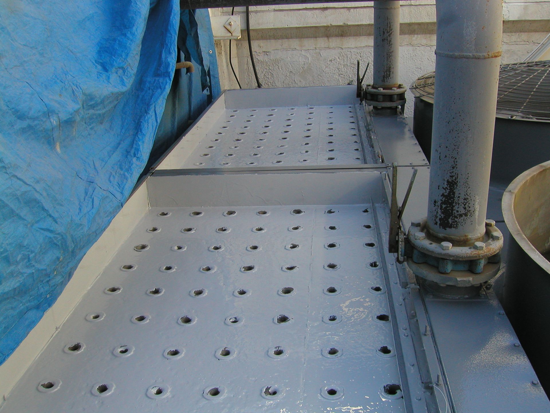 Blue covered industrial walkway with perforated metal platforms and vertical pipes