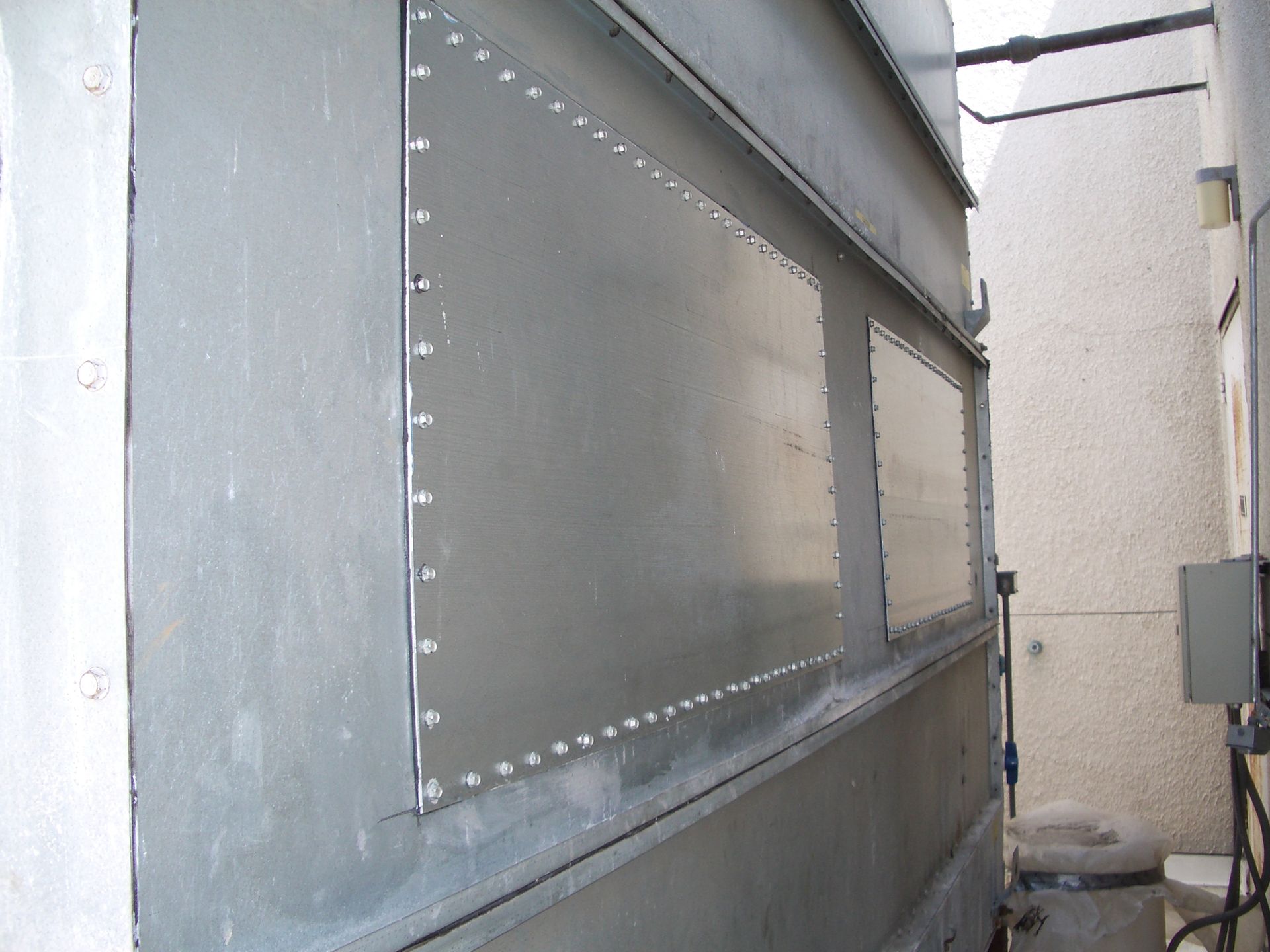 Metal panel mounted on a gray industrial wall with visible rivets and an inset rectangular window