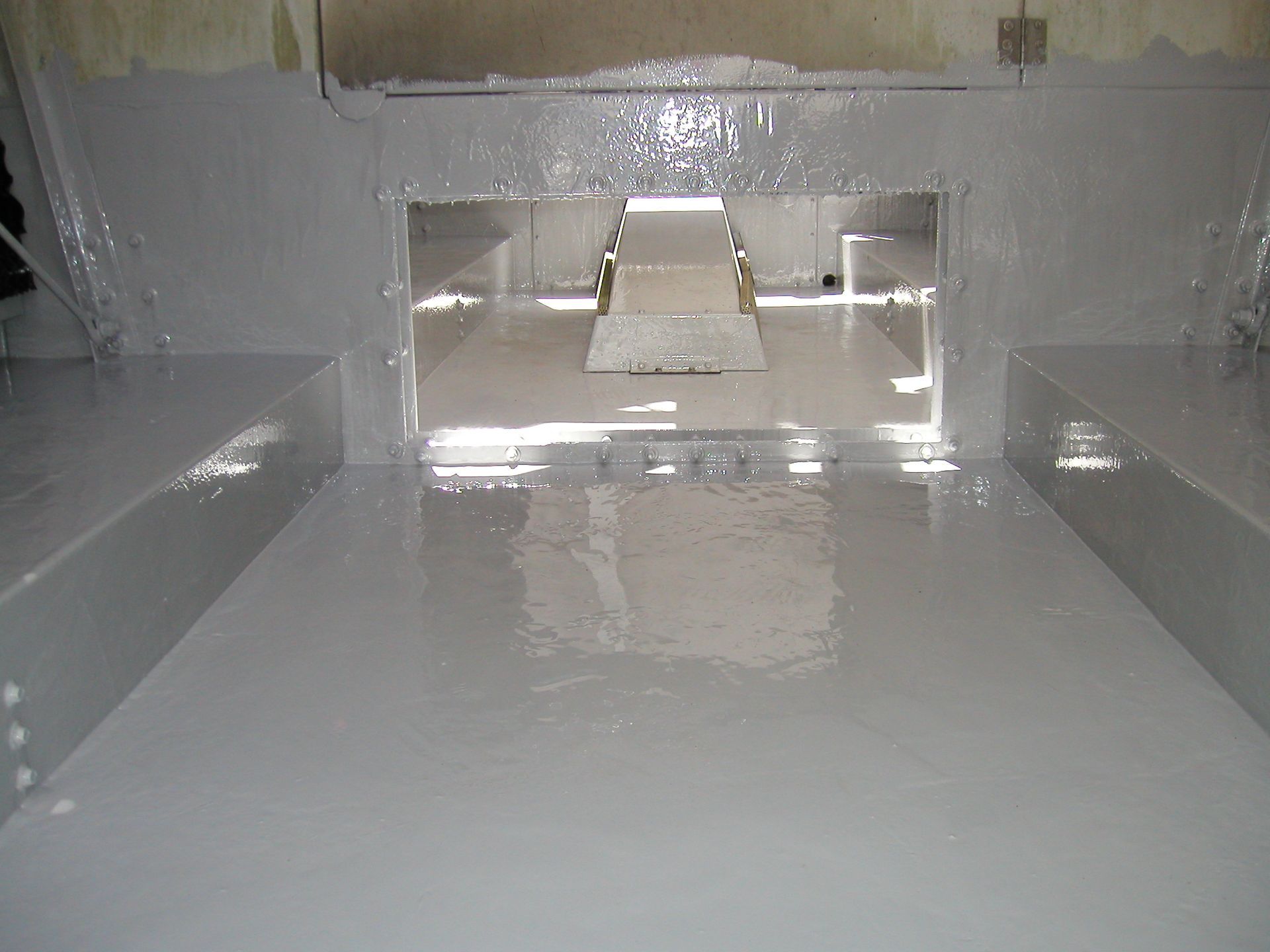 White industrial interior with a central ramp reflected on a glossy floor, viewed through an opening.
