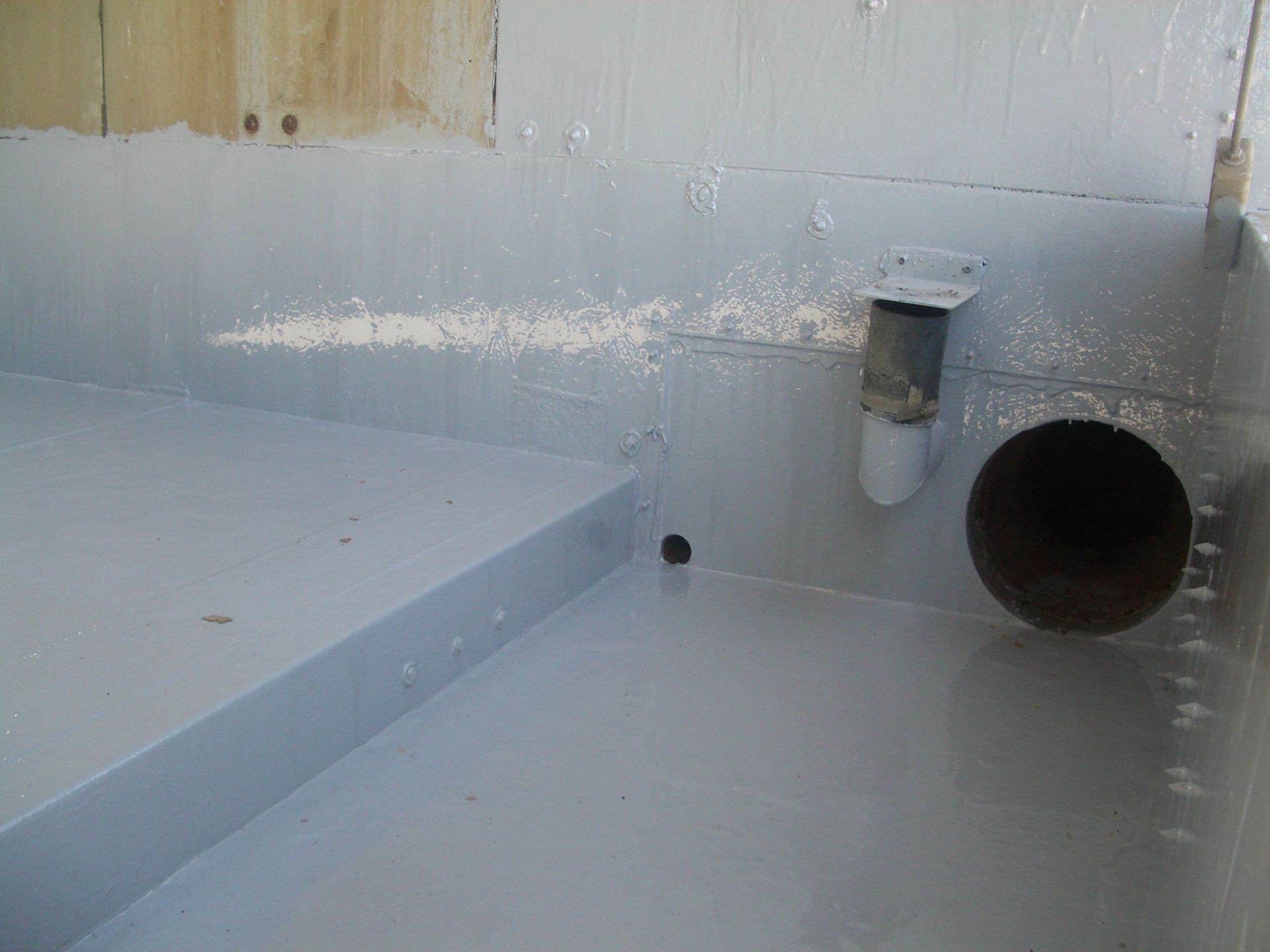 Gray waterproofed floor corner with pipes and a drain opening against a wall