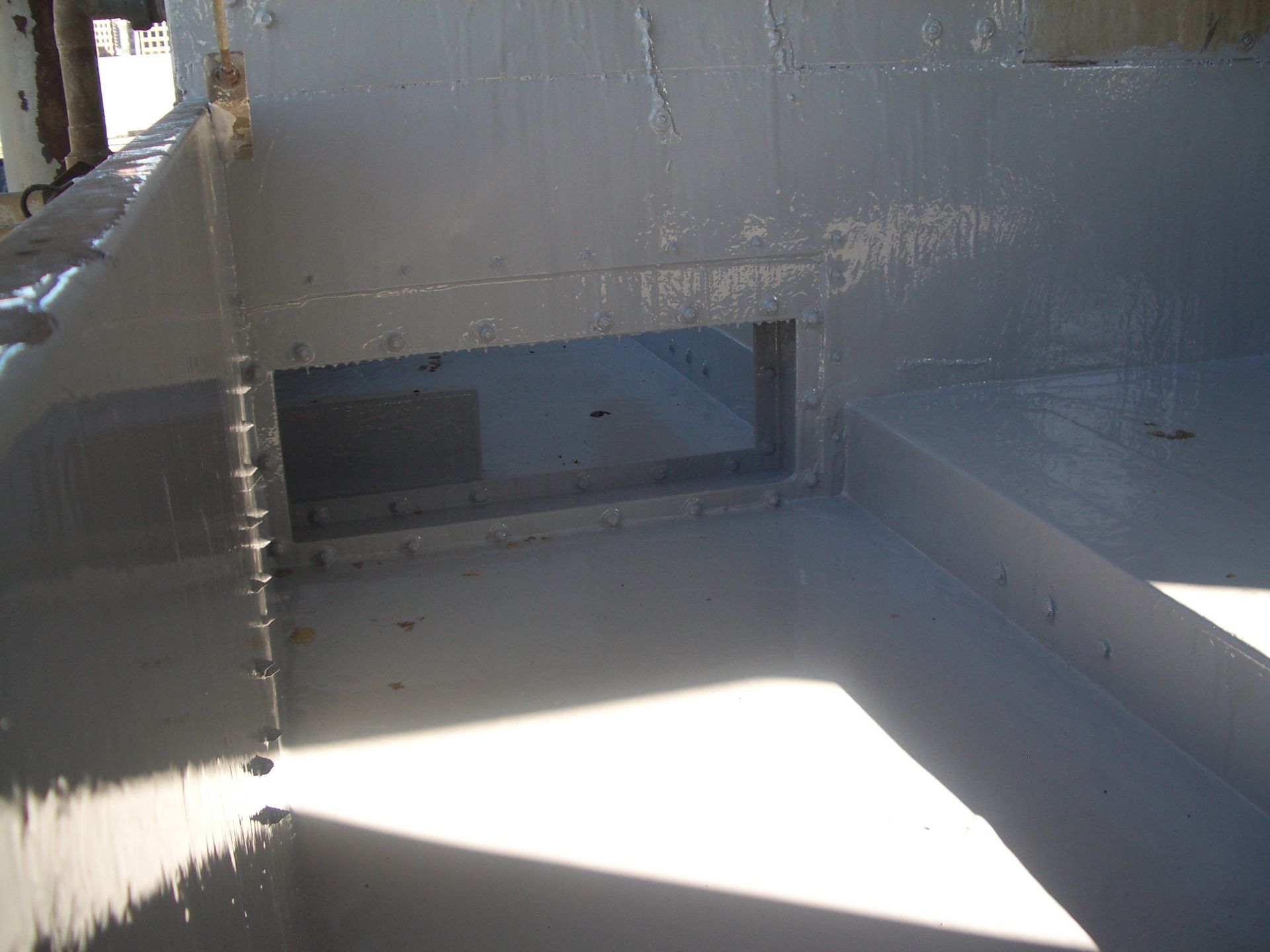 Gray industrial structure with a bright sunlit opening and a dark rectangular vent or slot.