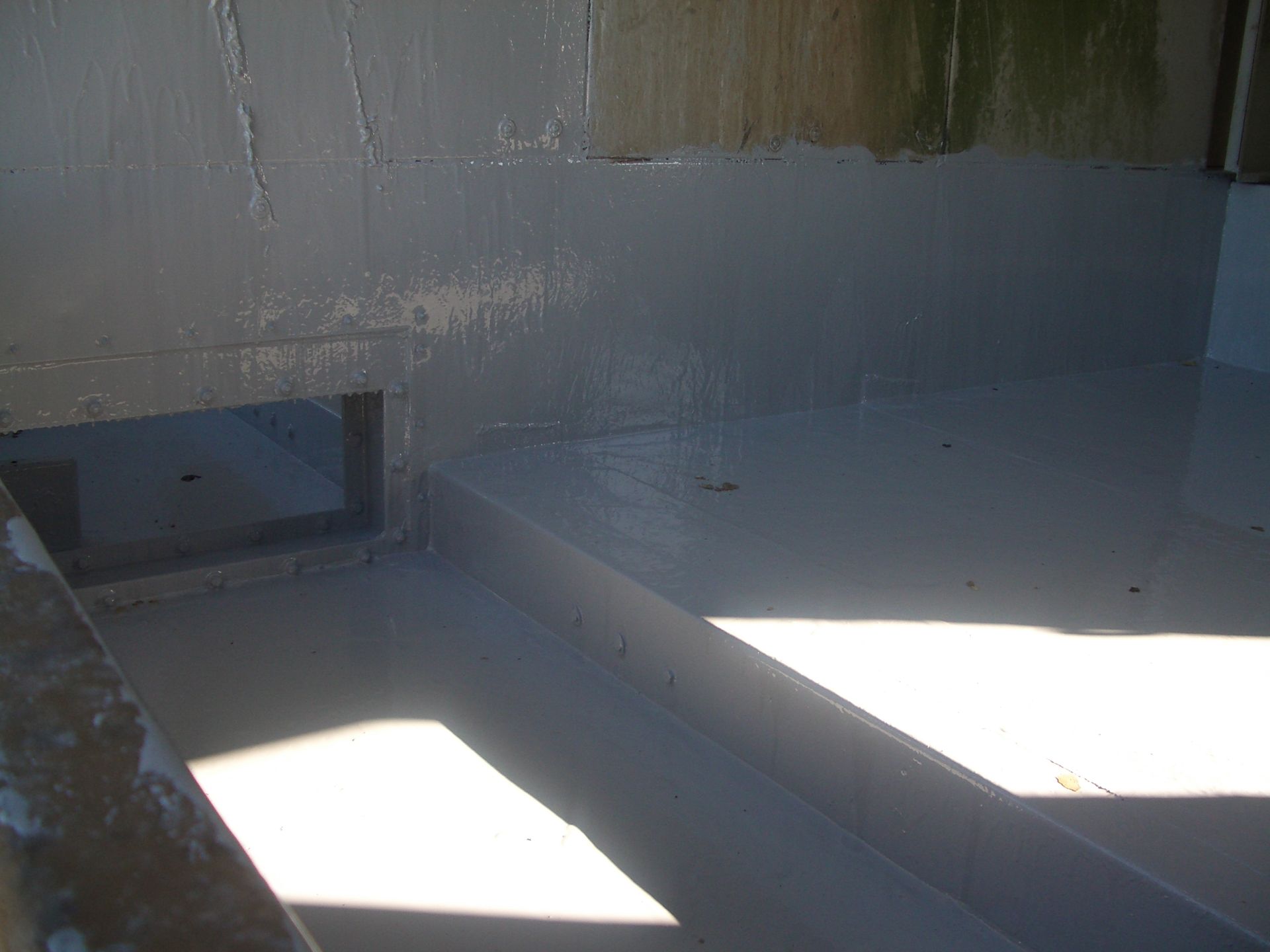 A white boat deck with bright sunlight, a small hatch, and a shadowed corner.