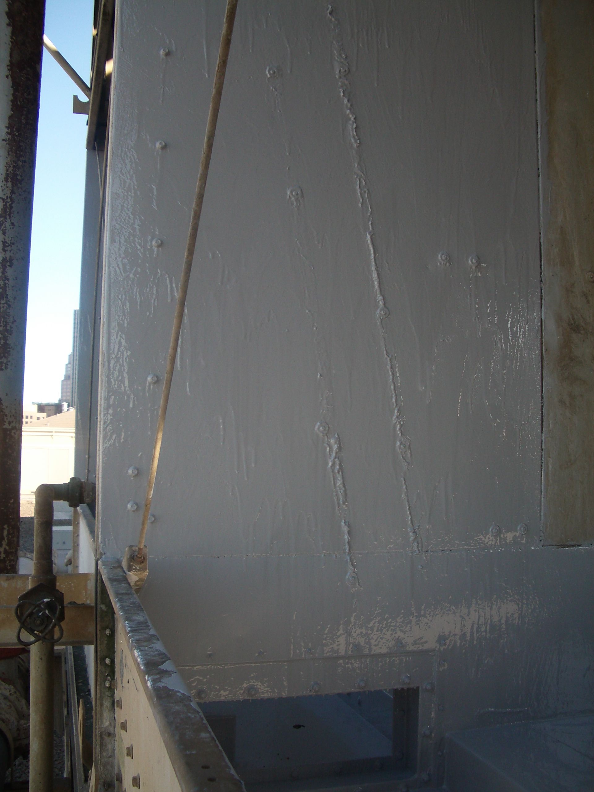 Gray painted wall with a small rectangular opening and a railing in front, outdoors in sunlight