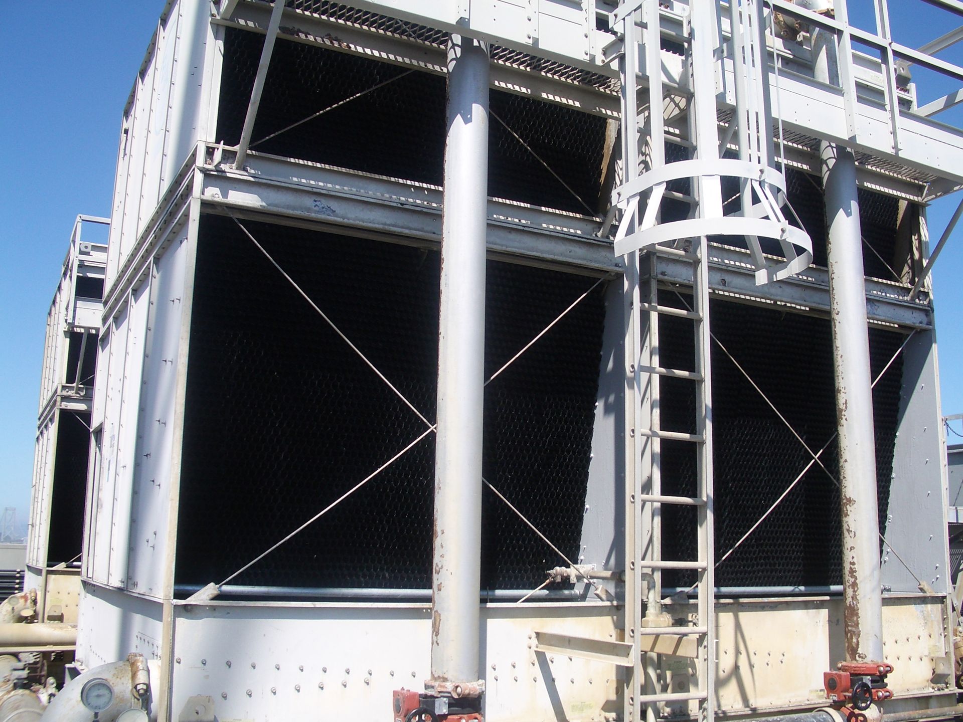 Industrial cooling tower under construction with steel framing, scaffolding, and white support columns