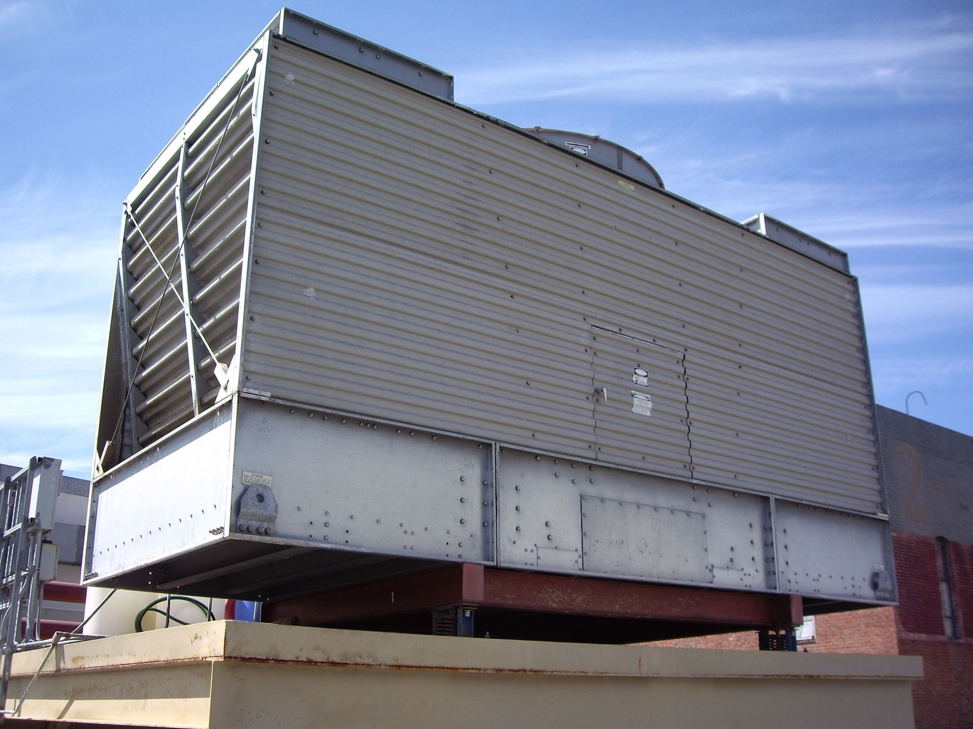 Large rooftop HVAC unit with metal vents and louvered panels on a brick building.