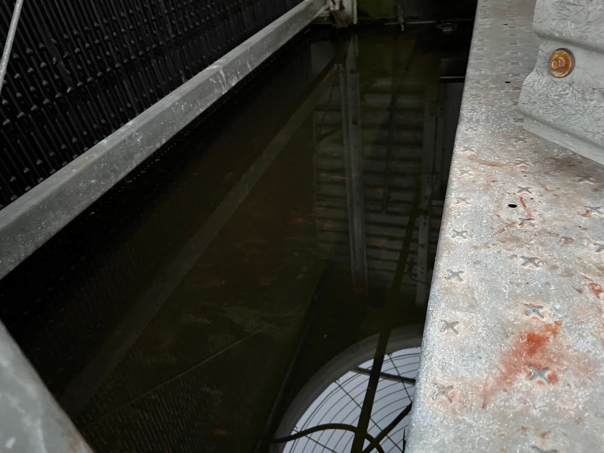 Dark water in a narrow concrete channel beside a metal fence and walkway with reflections.