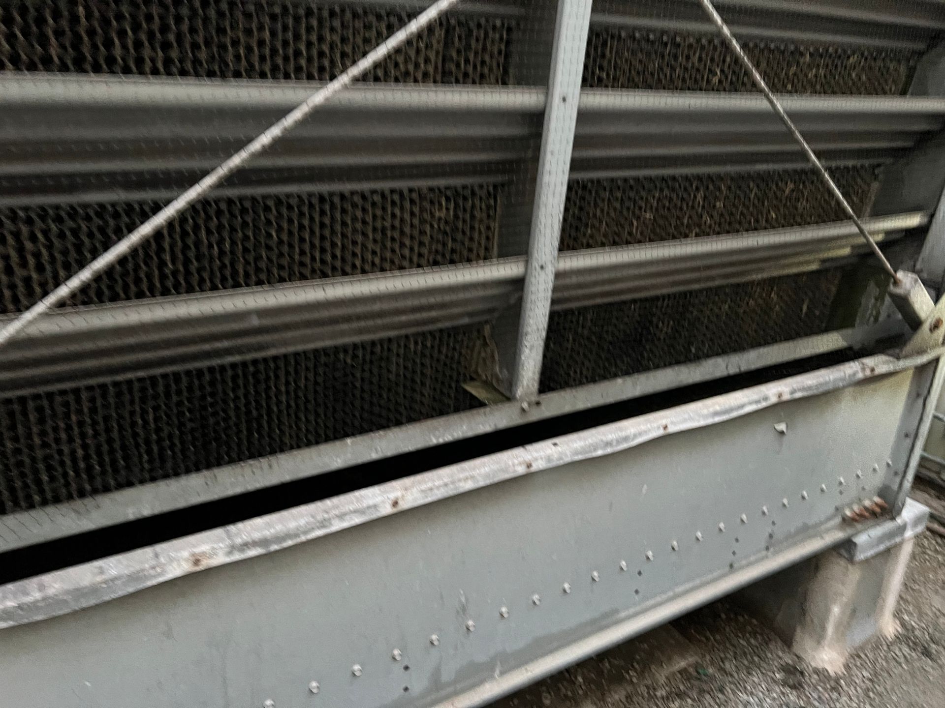 Gray metal beam and chain-link fence in an industrial setting, with diagonal support cables.