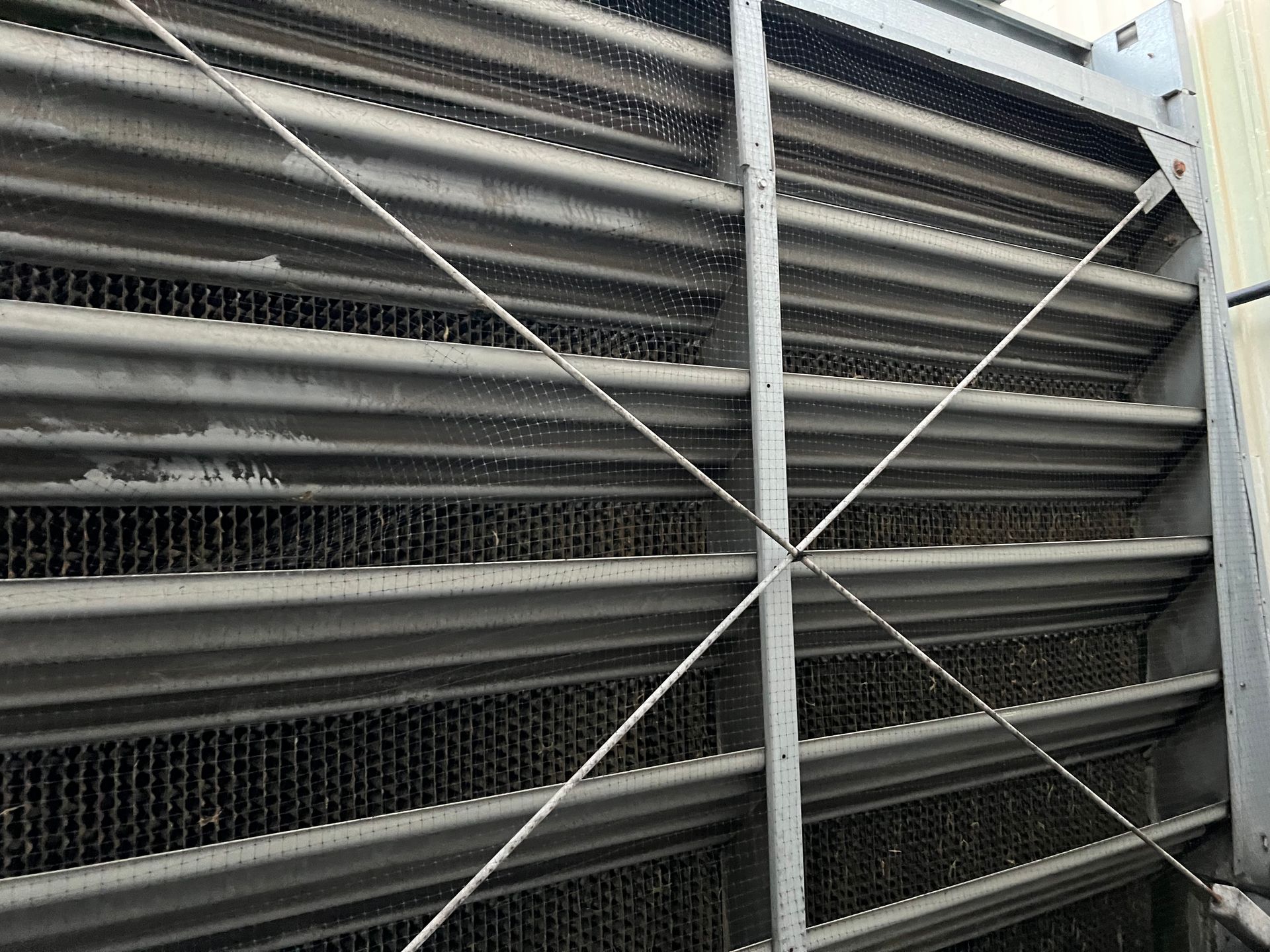 Close-up of a large gray metal ventilation louver with diagonal support wires