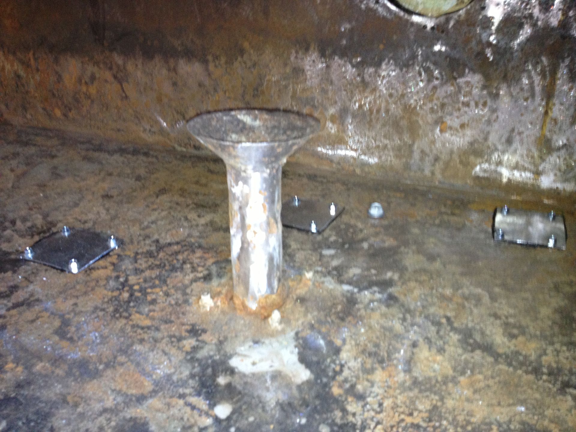 Rusty metal pipe in a wet, dirty industrial tank or basin with small objects nearby