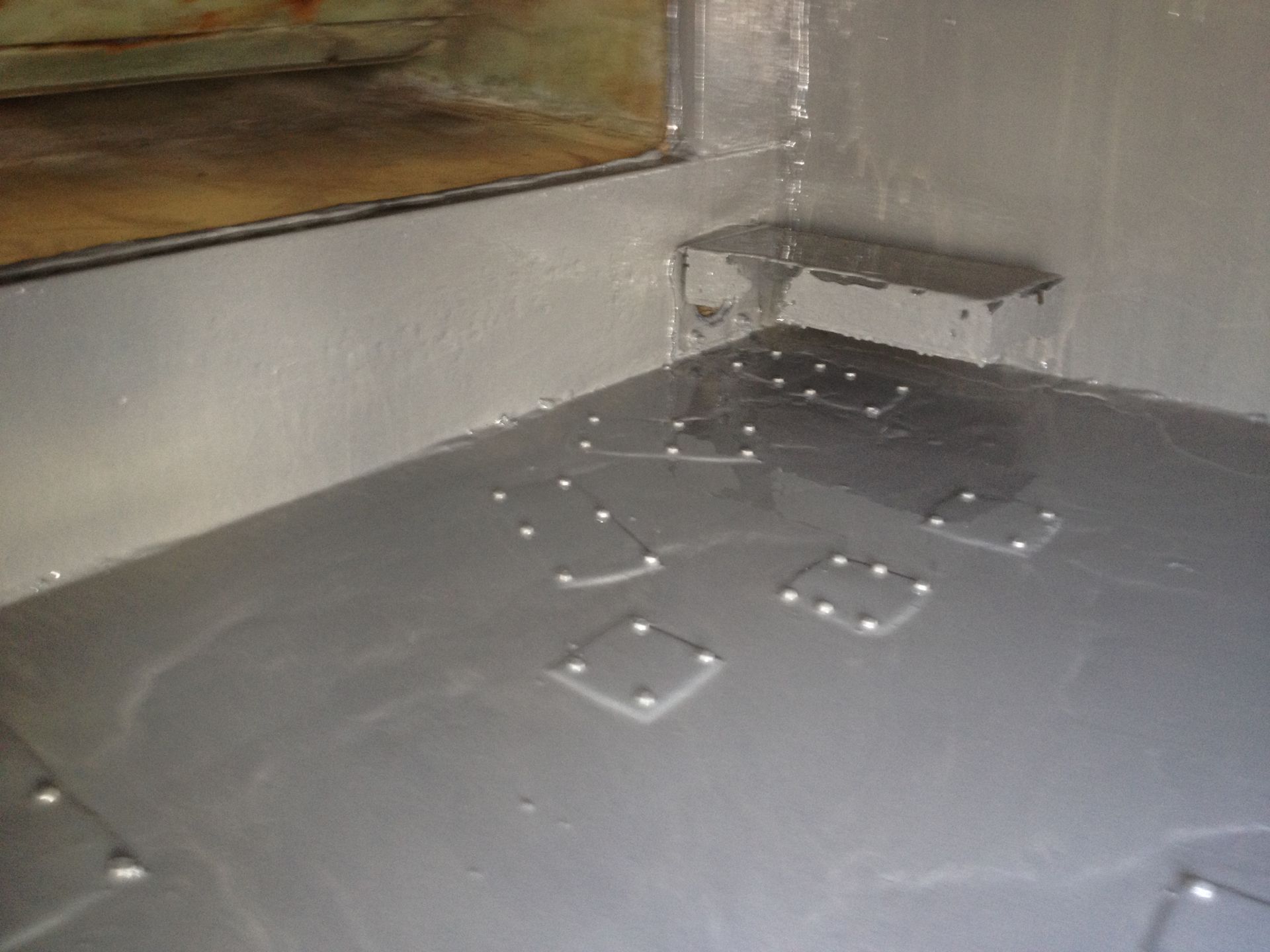 Gray indoor floor with scattered droplets and a small wall opening near a corner.