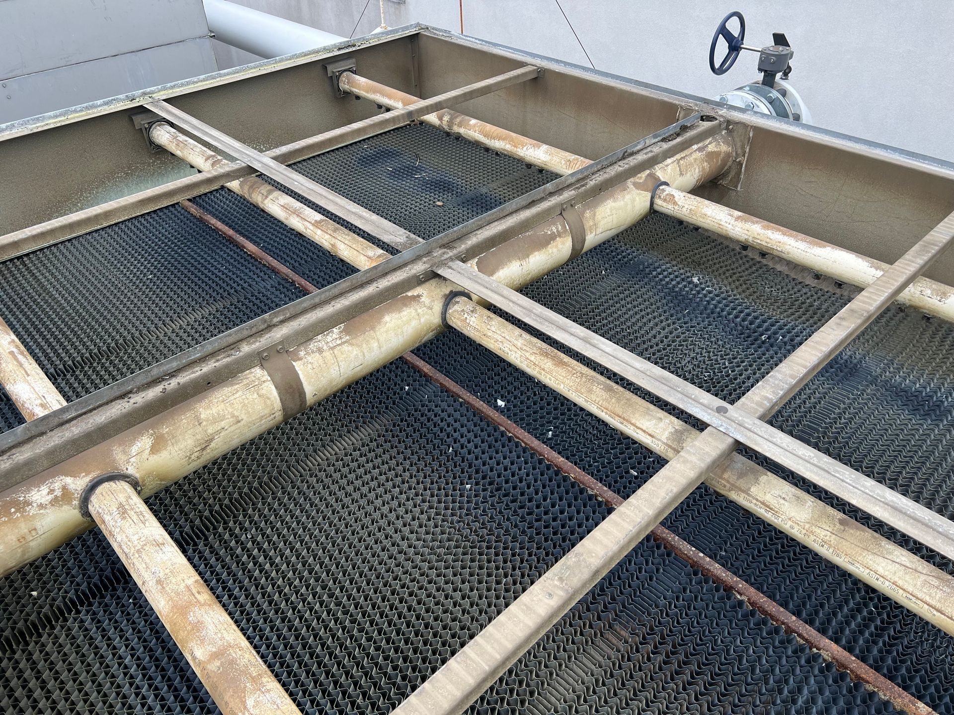 Industrial metal walkway with grated floors and beige pipes intersecting in a tank or utility area